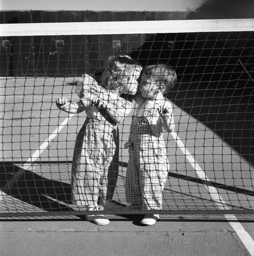 Vivian-Maier-Los-Angeles-Two-Children-Kissing-at-Tennis-Net-1955